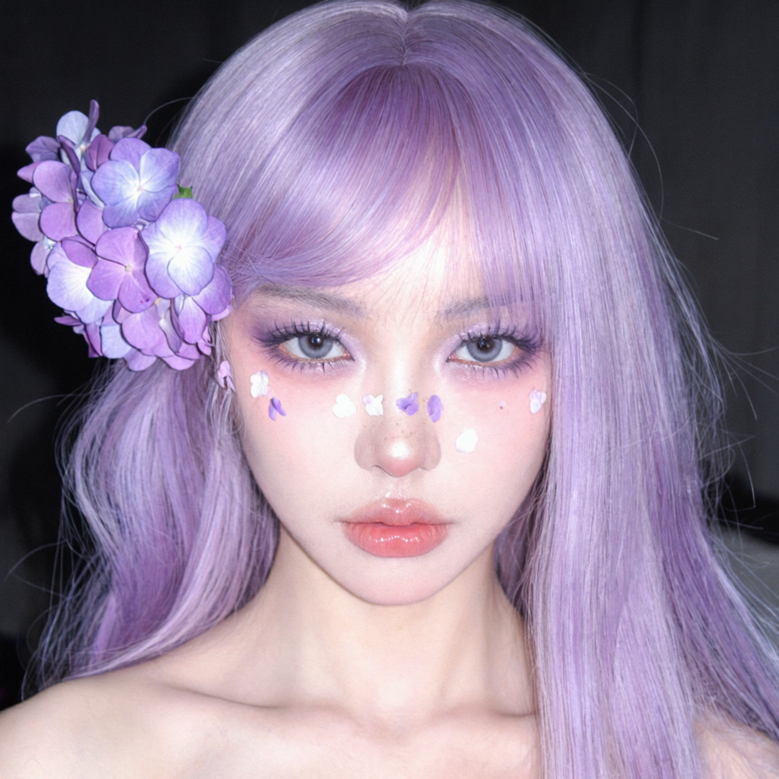 Amateur candid flash photography, raw unedited aesthetic, close-up portrait of a young East Asian woman with ethereal cosplay styling, extremely pale porcelain skin with hyper-detailed micro-texture, visible open pores on nose and cheeks, fine vellus hair (peach fuzz) on jawline, natural skin sheen, slight natural skin irregularities, distinct sharp collarbones with deep anatomical hollows, slender neck muscles tension, bare shoulders.

Hair: Voluminous pastel lilac wig, high-quality synthetic fiber texture with realistic stray hairs and messy flyaways catching the light, heavy blunt bangs covering forehead, large cluster of artificial purple hydrangea and lilac flowers pinned to the left side of the head.

Face & Makeup: Heavy violet and lavender eyeshadow gradient blown out around the eyes, thick spidery doll-like upper and lower lashes, grey-blue circle contact lenses with glassy reflection, painted white and purple flower petals artistically scattered across cheekbones and under-eye area, small button nose with intense specular flash highlight, plump glossy rose-pink lips with visible vertical lip lines, moisture texture, and slight parting.

Lighting & Technical: Harsh on-camera direct flash lighting (ring flash effect), pitch black void background, hard shadows cast behind the hair, high contrast, 35mm film grain, ISO 800, Fujifilm Superia simulation, f/2.8, slight chromatic aberration on edges, 8k resolution, photorealistic, unpolished, raw, intense gaze.