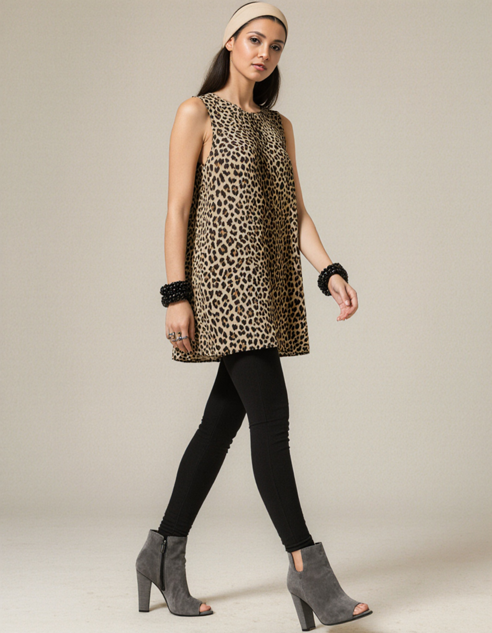 "A high-resolution Photo of a SaudiArabia woman.She wears a sleeveless, loose-fitting mini dress with a leopard print. The pattern is in natural tones (brown, beige, black) and is very striking, almost clichÃ©dly sexy. She pairs it with a black, tight-fitting leggings that completely cover her legs and give the look a touch of everyday wearability. She wears gray, open-toe high-heeled ankle boots with a cut-out for the toes â fashionable, but not overly glamorous. A wide, light-colored hairband holds back her hair with a center parting. The hairband gives her a somewhat youthful, almost naive look. She wears large black bracelets on both wrists, which serve as a fashion statement. She wears eye-catching rings on her left hand. Her makeup is rather subtle, with a focus on the lips and eyes â which fits well with her psychologically <lora:SaudiArabia:1>"