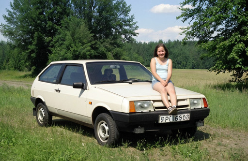 The photo shows a vaz 2108 parked in a grassy field, with a beautiful woman in a red sarafan standing in front of it. It's a hatchback with a LADA license plate. It has two doors and a roof rack, and appears to be in good condition, with no visible damage or wear. The field is surrounded by trees and bushes, and a hill is visible in the background. The sky is blue, giving the overall mood of the image a peaceful and serene feel., amateur photo from 2003, candid snapshot, early 2000s aesthetic, compact digital camera look, realistic old consumer camera quality, slight grain, soft direct flash, low dynamic range, nostalgic atmosphere, casual composition, imperfect framing, authentic family photo vibe, subtle motion blur, washed colors, natural skin texture, indoor evening lighting, early digital photography artifacts, cozy mood, unedited look, realistic amateur photography, point and shoot camera, ccd sensor look, jpeg compression artifacts, chromatic noise, low resolution digital photo, eastern european atmosphere, post soviet aesthetic, 2000s urban environment, cheap digital camera, low end point and shoot, old cybershot camera quality<lora:Lada (VAZ)_2108_lora_XL:1>